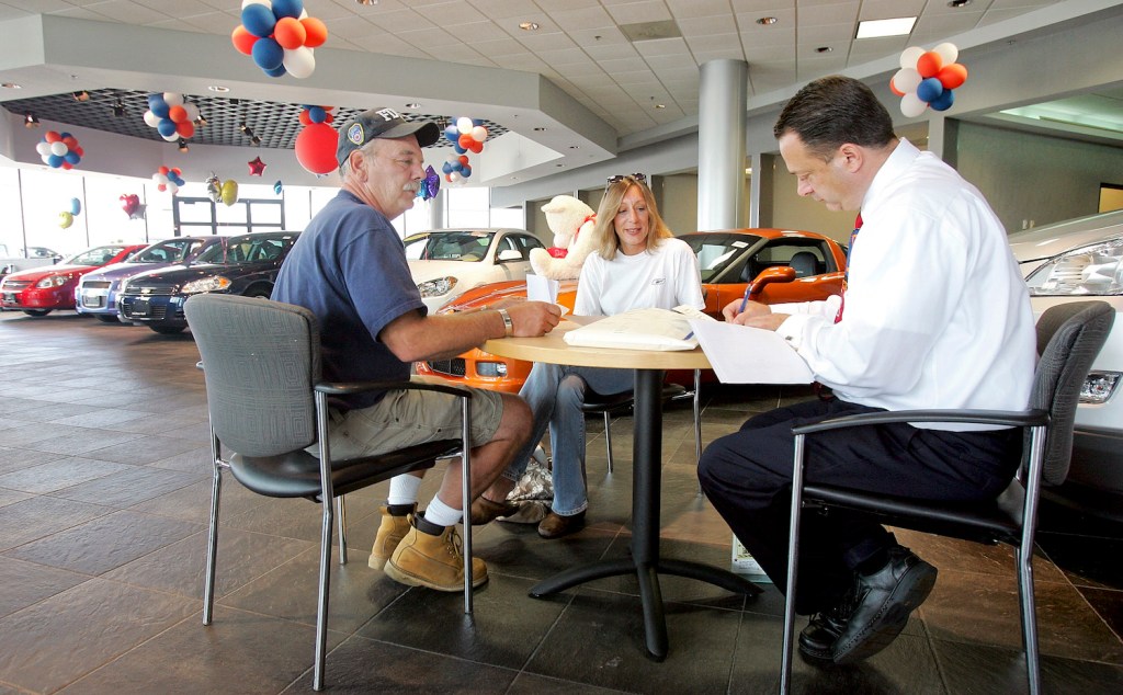 A couple sitting across from a car salesman while shopping for a car.