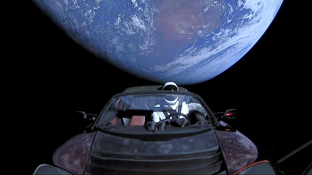 A Tesla Roadster floats in space piloted by a mannequin in a space suit