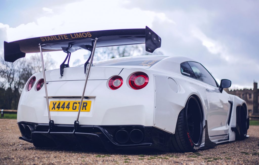 The rear 3/4 view of the black-and-white Starlite Limos' R35 Nissan GT-R with a Rocket Bunny body kit parked by an English countryside manor
