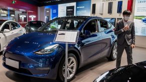 A vendor stands next to a blue Tesla Model 3 car on display at a shopping mall in Beijing