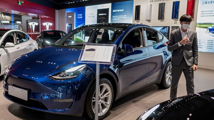 A vendor stands next to a blue Tesla Model 3 car on display at a shopping mall in Beijing