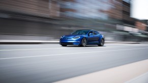 A blue Tesla Model S travels on a multilane city highway