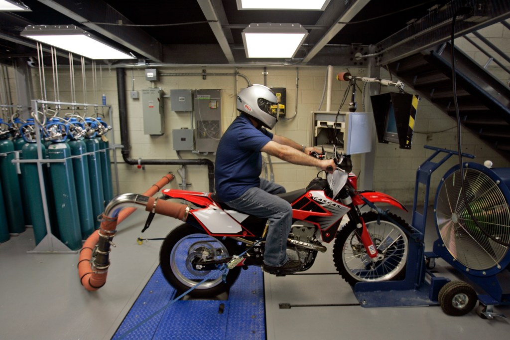 A rider emissions testing a red Gas Gas FSR 450 on a CARB motorcycle dynamometer