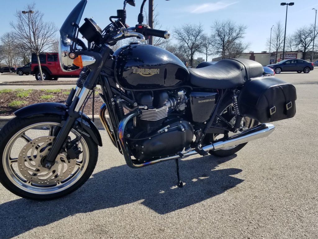 The side 3/4 view of a black 2009 Triumph Bonneville with saddlebags rented on Twisted Road in a parking lot