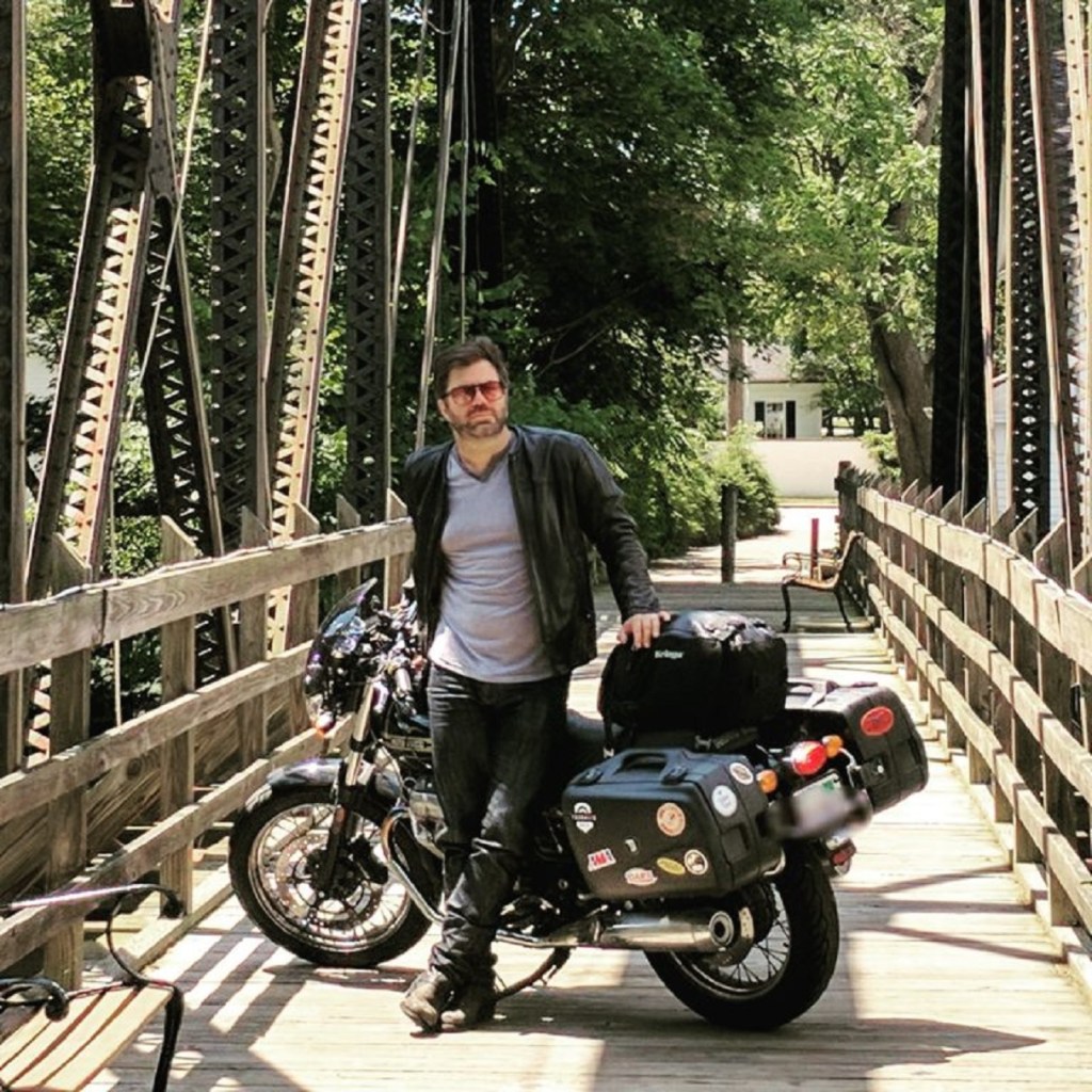 Twisted Road founder Austin Rothbard with his black-and-gold 2010 Moto Guzzi V7 Classic on a bridge