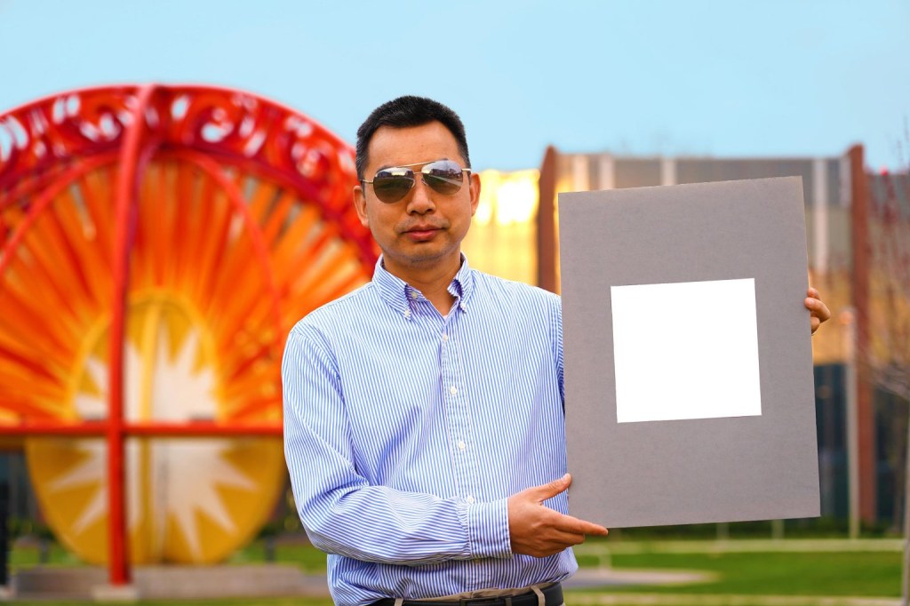 Xiulin Ruan standing with a sample of the whitest white paint