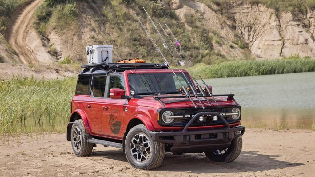 2021 Ford Bronco in red covered in fishing gear pared next to a pond