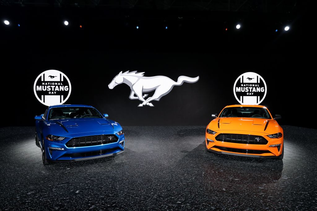 A blue Ford Mustang and orange Ford Mustang on display with a contrasting black backdrop