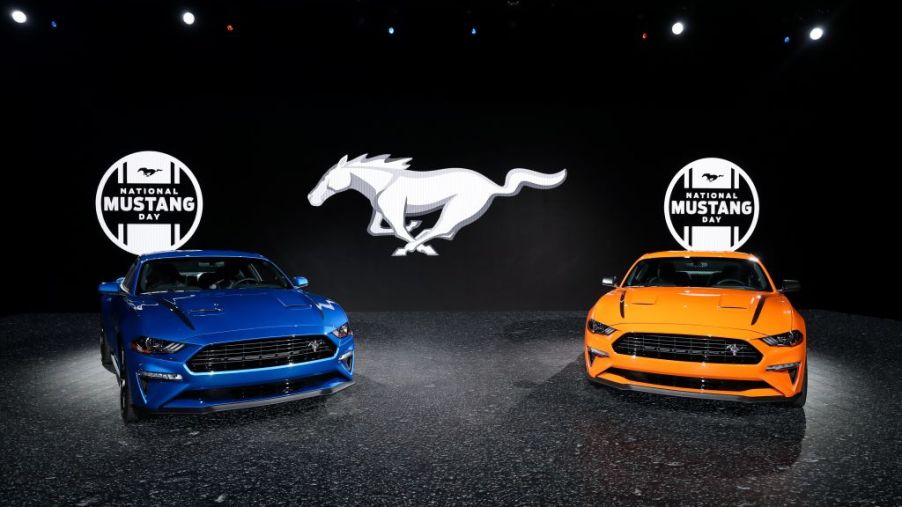A blue Ford Mustang and orange Ford Mustang on display with a contrasting black backdrop