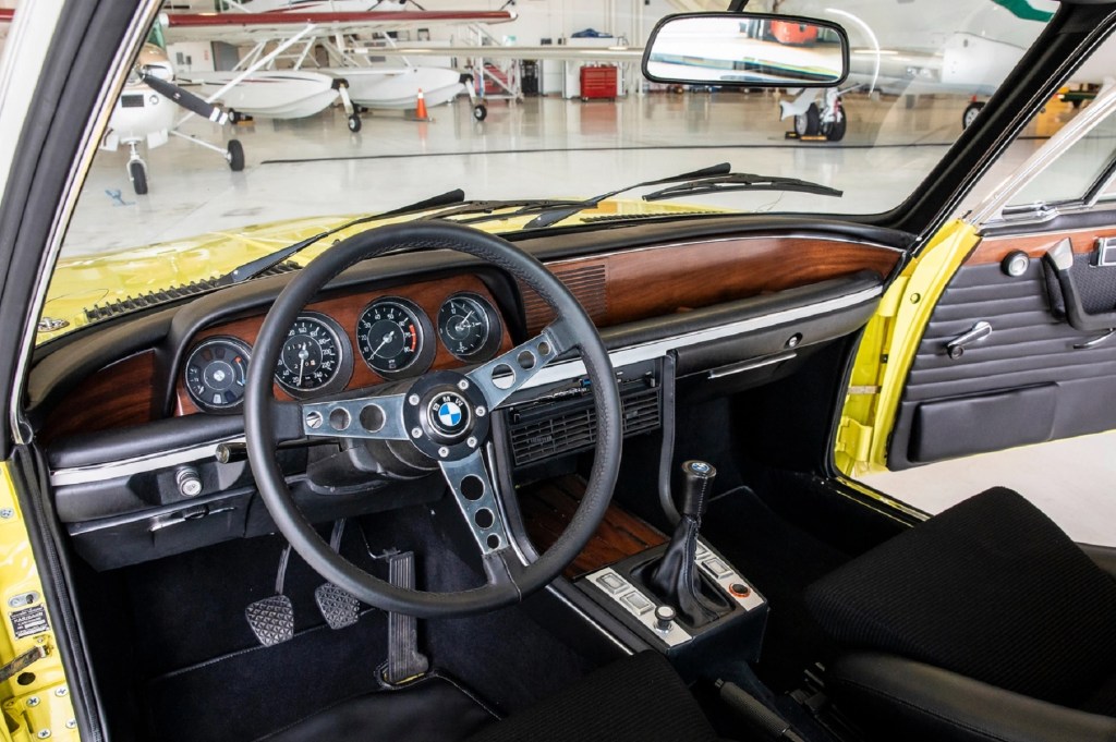 The black-leather front seats and wood dashboard of a yellow 1973 BMW 3.0 CSL