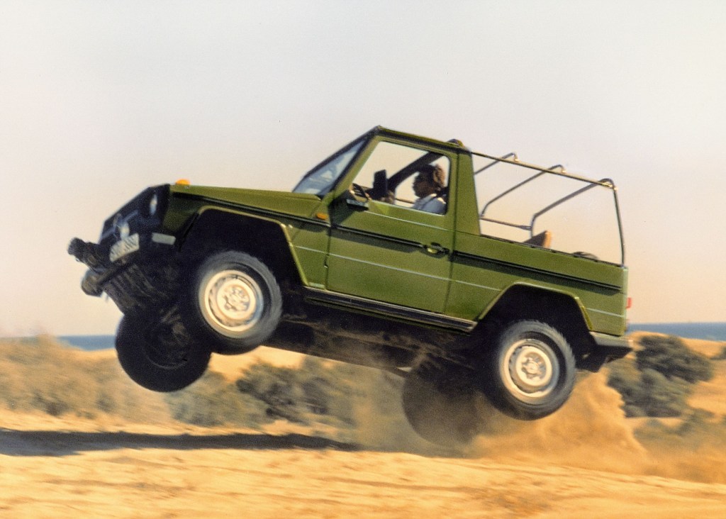 A green 1979 Mercedes G-Wagon Convertible jumping over sand