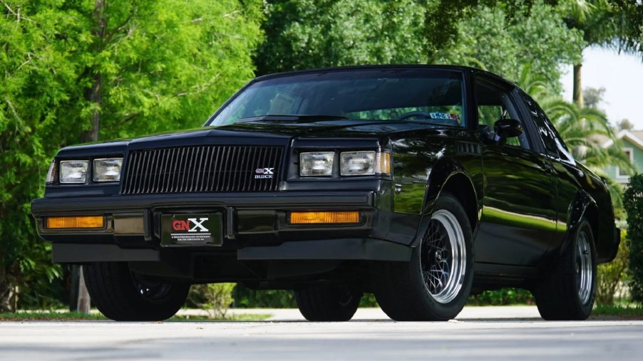 The front 3/4 view of a 262-mile black 1987 Buick GNX in a tree-lined parking lot