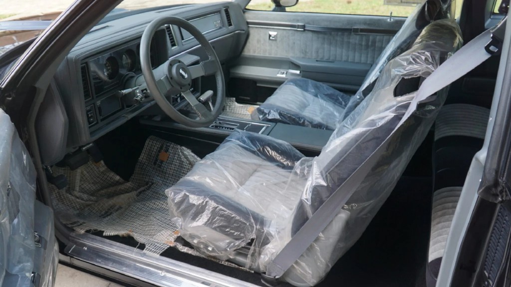 The gray-and-black front interior of a 1987 Buick GNX with the factory plastic seat wrapping