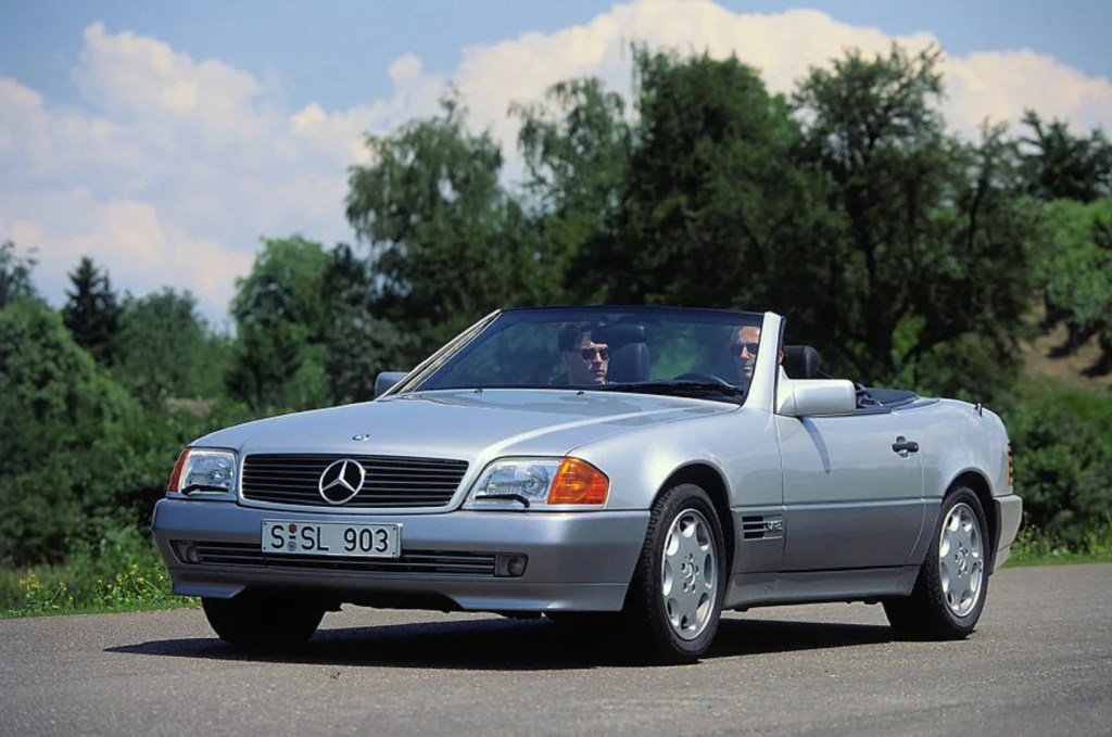 A two-tone silver-and-gray 1992 R129 Mercedes-Benz 600 SL driving down a country road