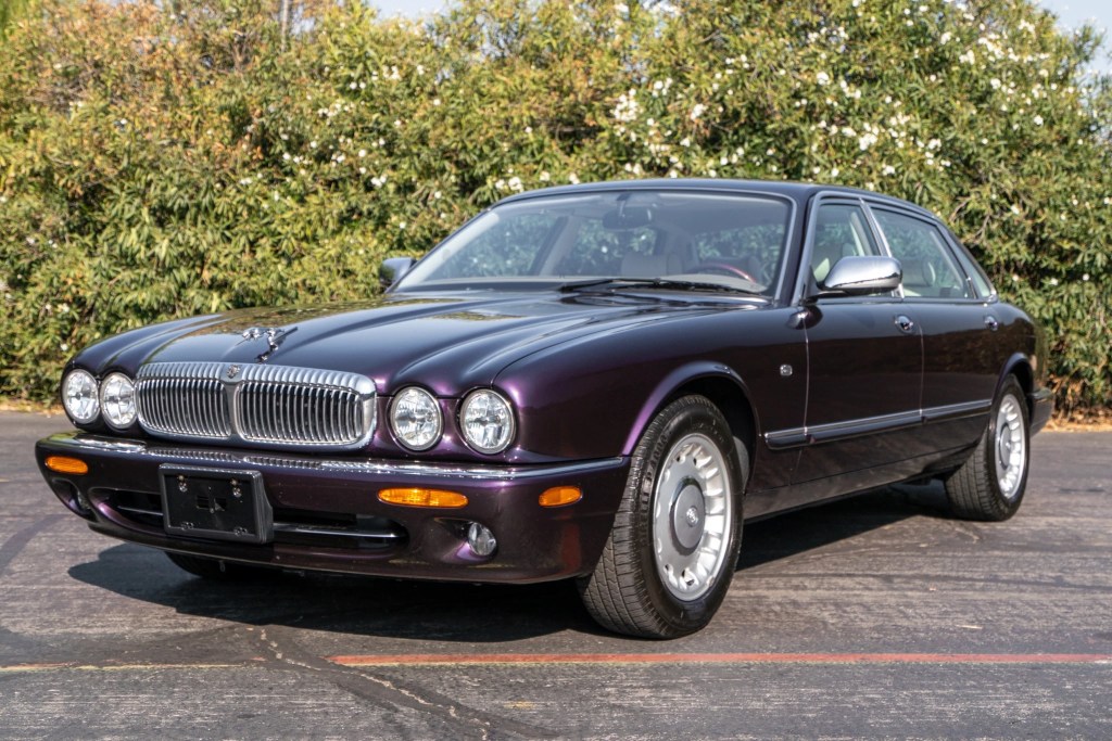 The front 3/4 view of a purple 1998 Jaguar XJ Vanden Plas in front of a hedge