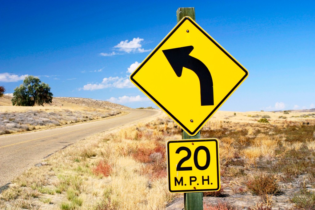 Road in Idaho, USA, warning to reduce speed to 20 miles per hour while rounding the curve.