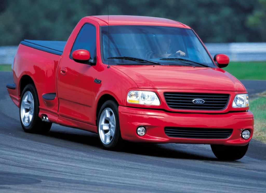 A red 2001 Ford F-150 SVT Lightning drives around a corner of a racetrack