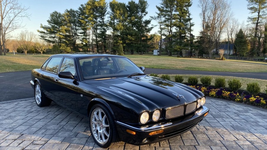 A black 2002 Jaguar XJR 100 on a stone driveway in front of a tree-lined lawn