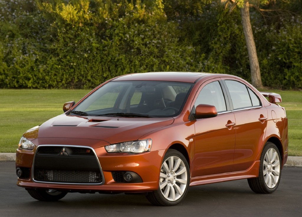 An orange 2009 Mitsubishi Lancer Ralliart parked by a hedge-lined lawn