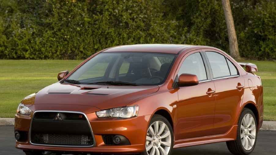 An orange 2009 Mitsubishi Lancer Ralliart parked by a hedge-lined lawn