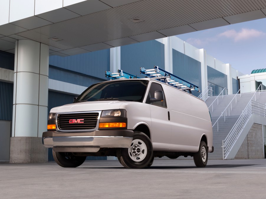A white 2014 GMC Savana cargo van parked next to a modern white building