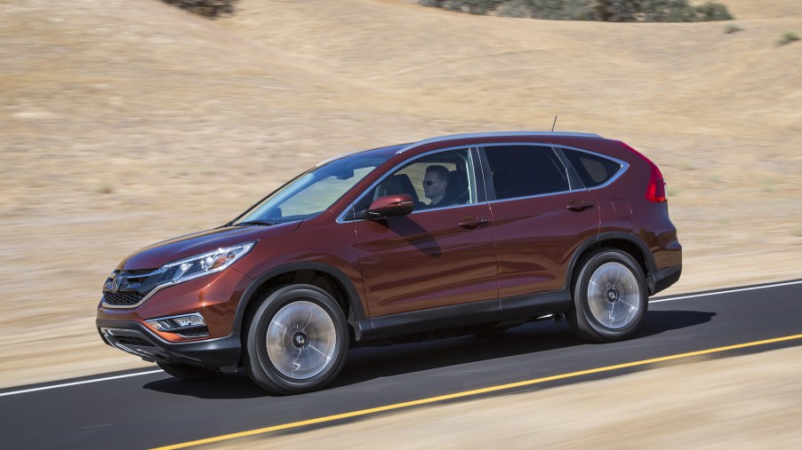 A dark-red metalllic 2016 Honda CR-V compact SUV travelinig on a road past hills with dry brown grass