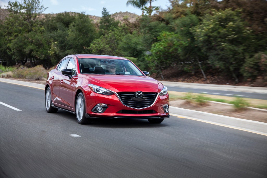 The red 2016 Mazda3 rolls down the road with trees passing in a blur in the background