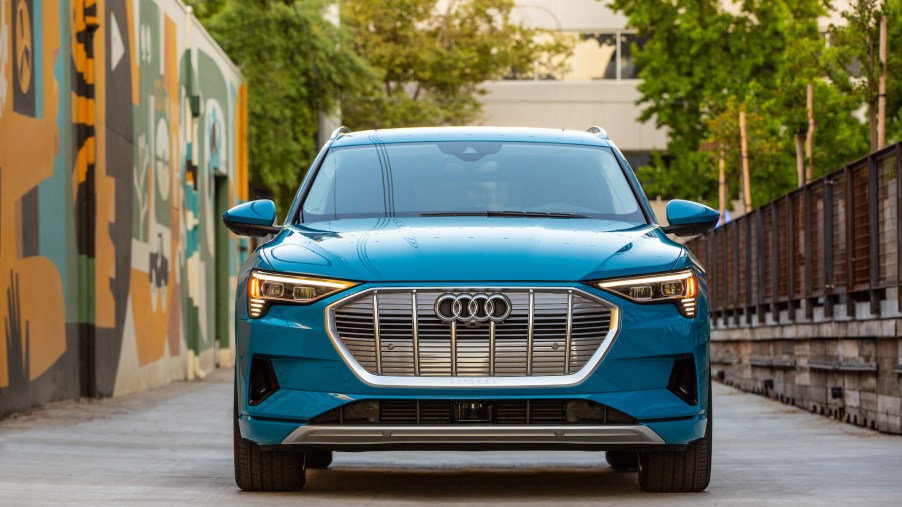 Front view of a turquoise-blue 2019 Audi e-tron electric SUV parked next to an abstract mural in a city