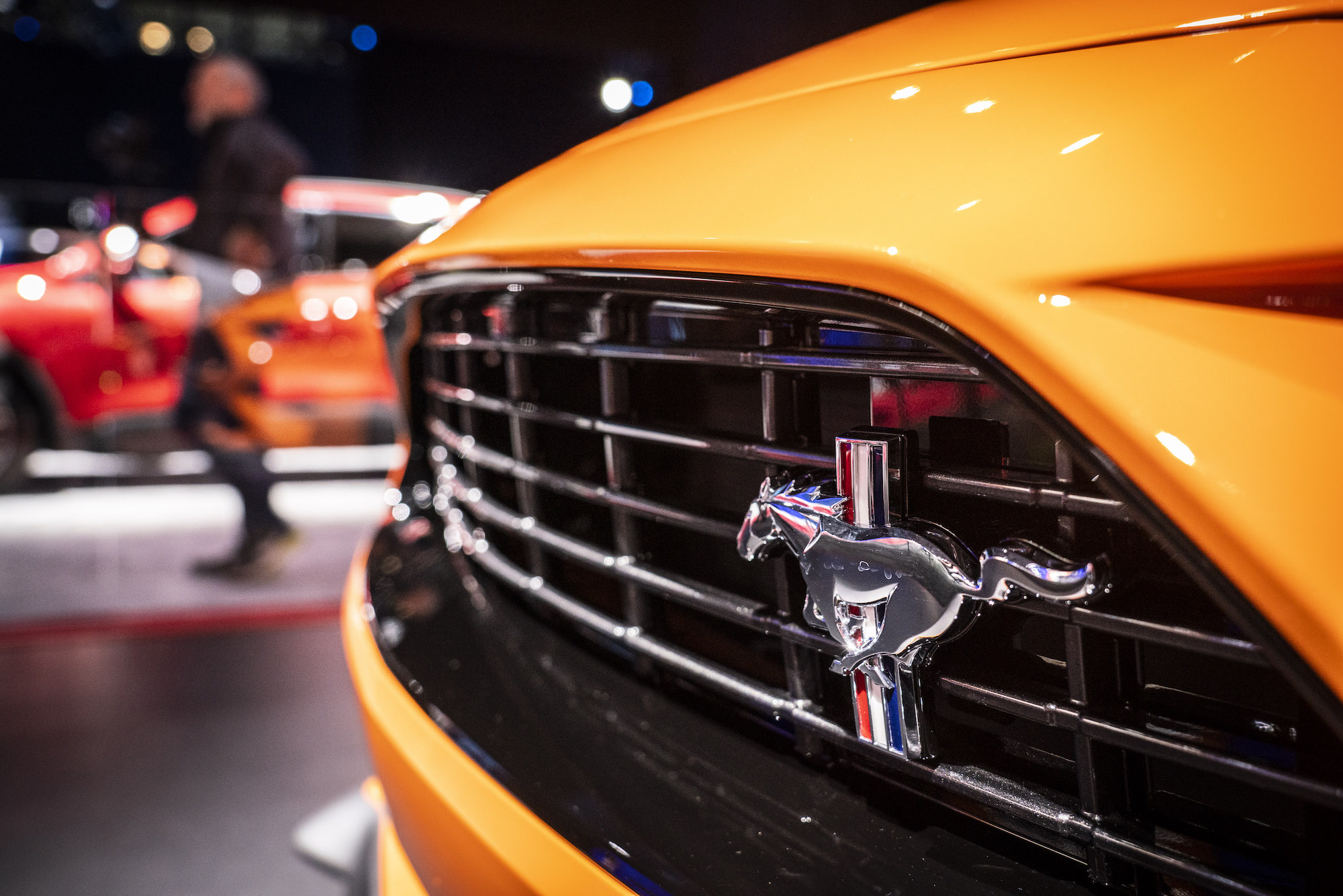 A logo is displayed on the grille of an orange Ford Mustang at the 2019 New York International Auto Show