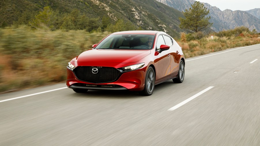 A red 2019 Mazda3 hatchback traveling on a highway past dry grass and mountains