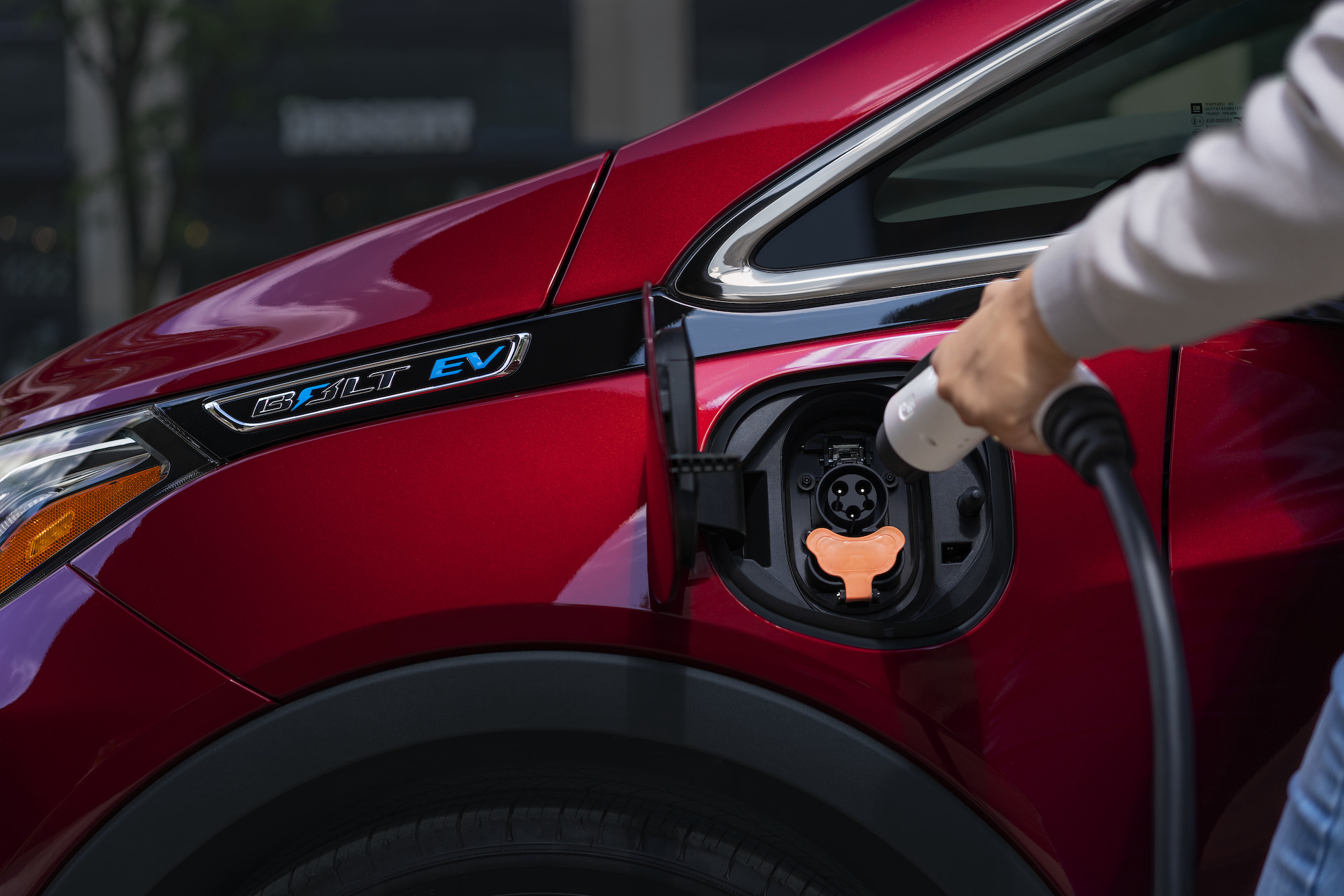 A person charges a red 2020 Chevrolet Bolt EV