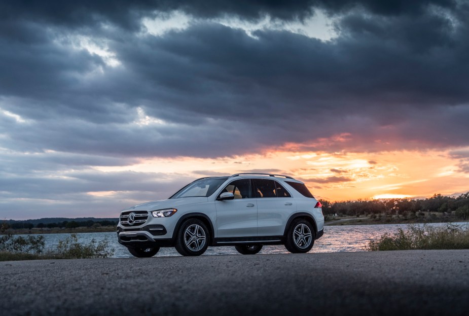 A white 2020 Mercedes-Benz GLE midsize luxury SUV parked overlooking a body of water with dark clouds overhead and the sun on the horizon