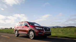 A red 2020 Subaru Ascent midsize SUV traveling on a rural road on a sunny day