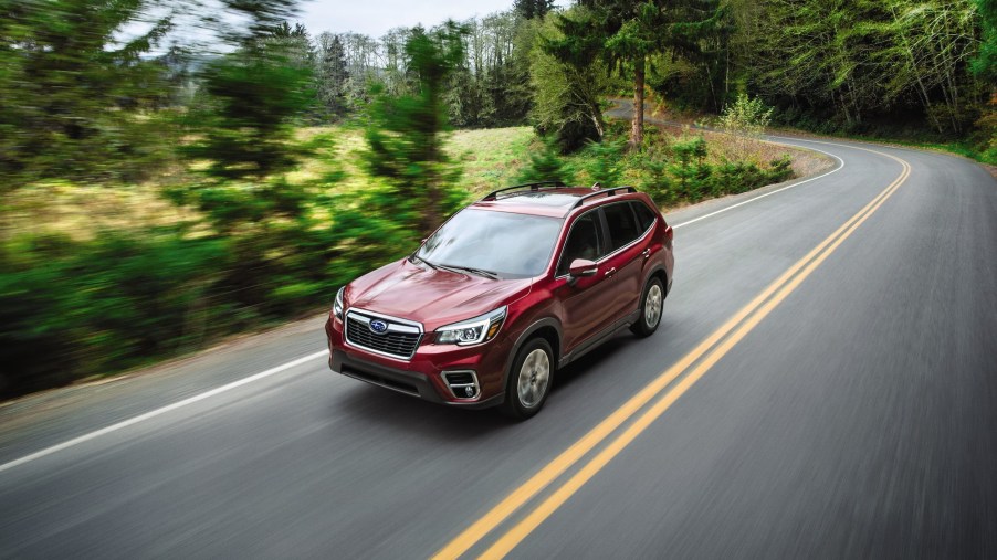 A dark-red 2020 Subaru Forester traveling on a two-lane highway through lush trees