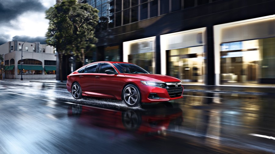 A red 2021 Accord Sport 2.0T midsize sedan travels on a wet city street on a cloudy day