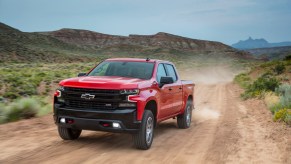 A red 2021 Chevrolet Silverado LT Trail Boss travels on a dirt road past mountains