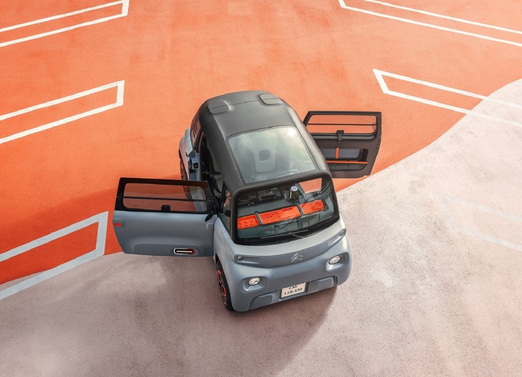 An overhead view of a gray 2021 Citroen Ami with its doors open on a gray-and-orange concrete surface