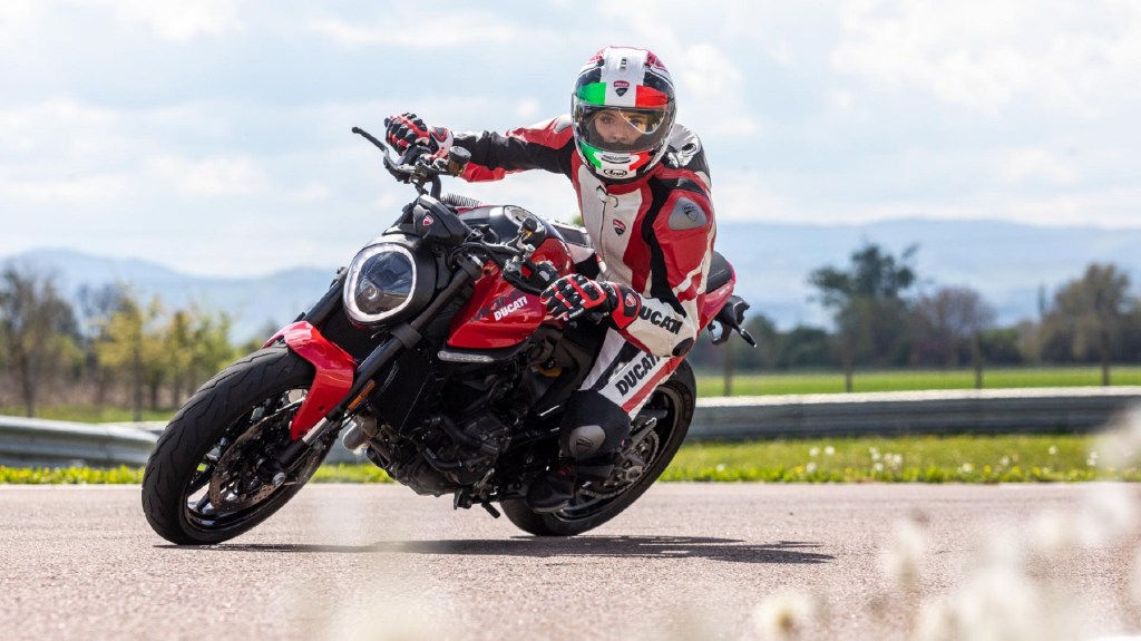 A red-and-white-clad rider takes a red 2021 Ducati Monster around the corner of a racetrack