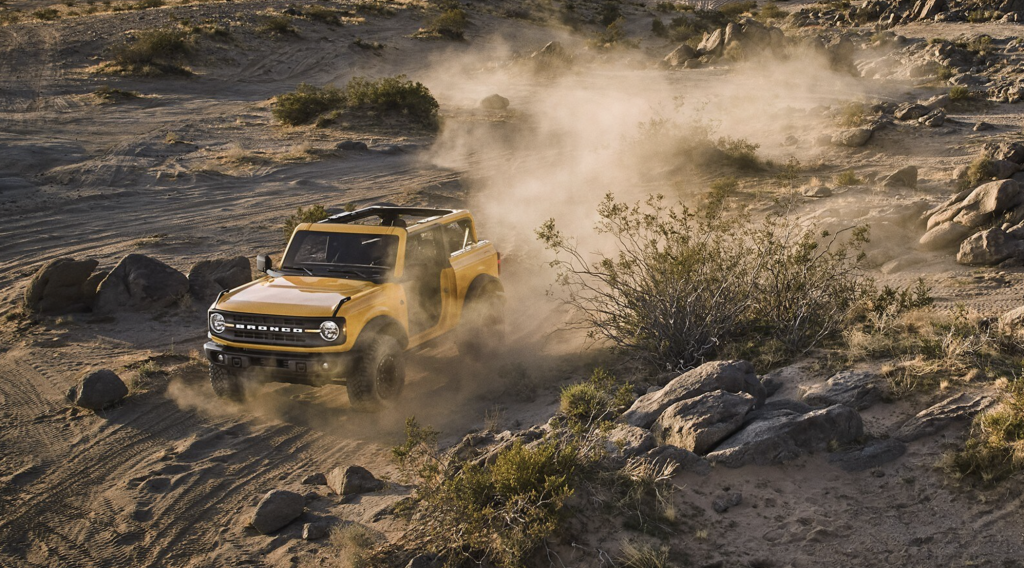 A yellow 2021 Ford Bronco driving through the desert on a dirt road