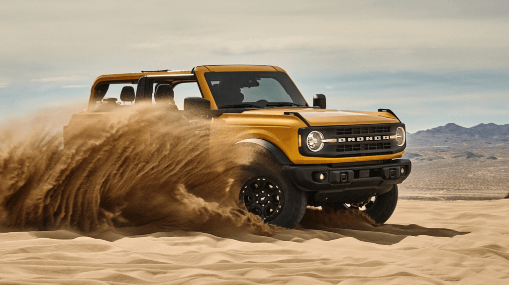 A yellow 2021 Ford Bronco SUV kicking up a door-height wave of sand in the desert