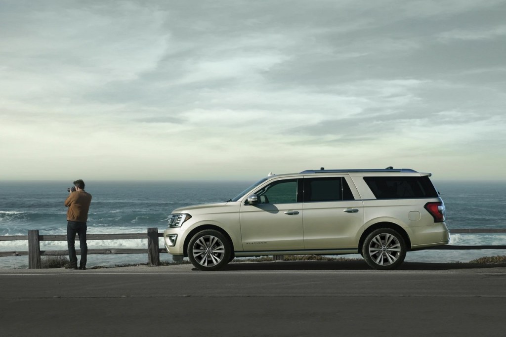 The safest large SUV, a Ford Expedition, sits in front of the ocean while a man takes photos.