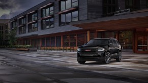 A black 2021 GMC Acadia Elevation midsize SUV parked in front of a brown modern building