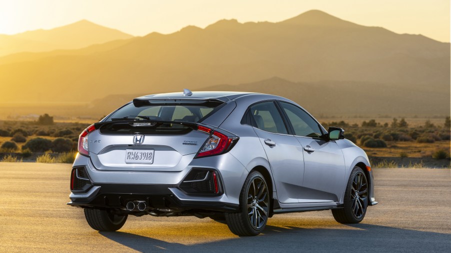 A silver 2021 Honda Civic Hatchback Sport Touring parked in front of mountains and the sun