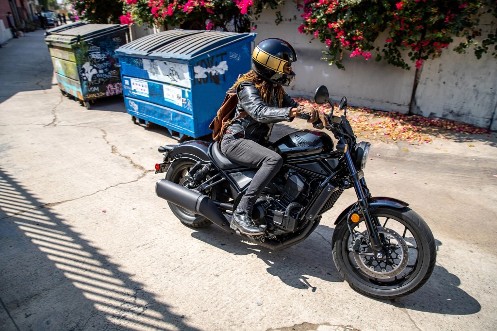 A rider with a black-and-gold helmet takes a black 2021 Honda Rebel 1100 DCT through an alleyway