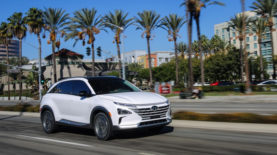 A white 2021 Hyundai Nexo compact crossover SUV traveling on a city street lined with palm trees