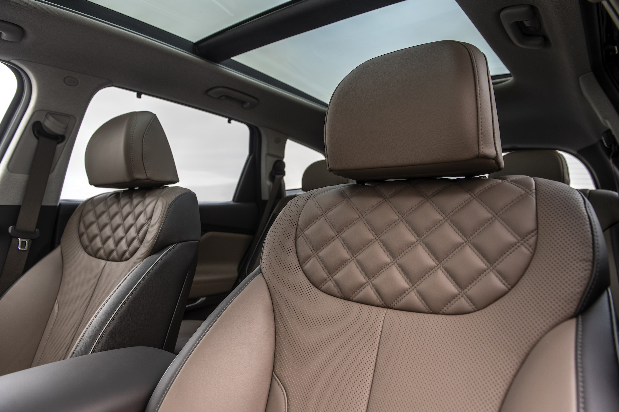 An interior photo of the tan leather front seats and panoramic sunroof of a 2021 Hyundai Santa Fe midsize SUV