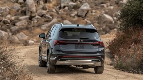A rear view of a dark-gray 2021 Hyundai Santa Fe midsize SUV on a mountain road