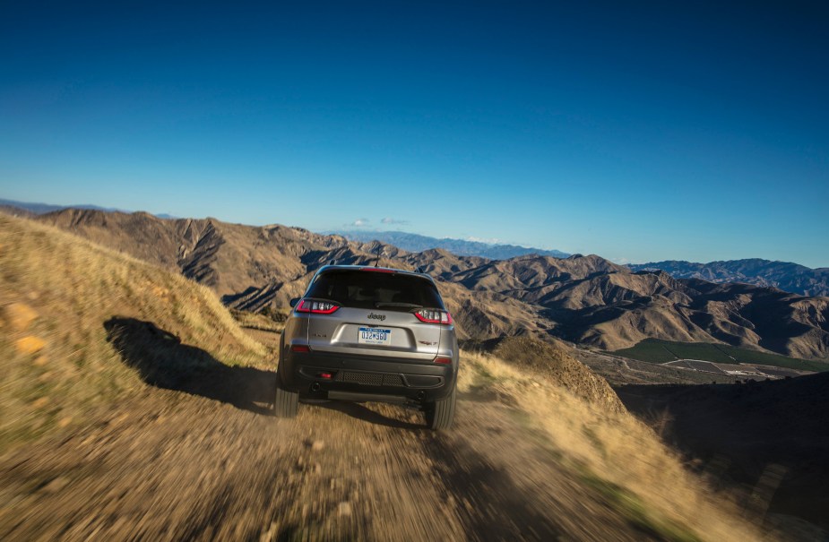 A rear view of a 2021 Jeep Cherokee Trailhawk traveling over gravel on a mountain