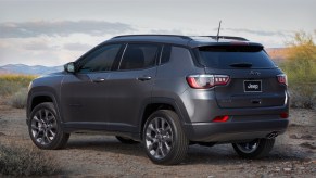 A dark-gray metallic 2021 Jeep Compass 80th Anniversary Edition compact crossover SUV parked on gravel in front of mountains in the distance