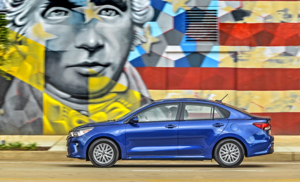 A blue 2021 Kia Rio driving past a mural